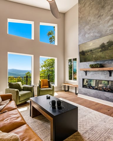 Modern living room with leather sofa, fireplace, mountain views through floor-to-ceiling windows and glass doors to balcony