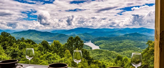 Dining table with place settings overlooking forested mountains and river valley under cloudy sky