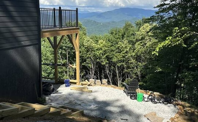 Modern black cabin with elevated wooden deck overlooking forested mountains and valley under blue sky with clouds